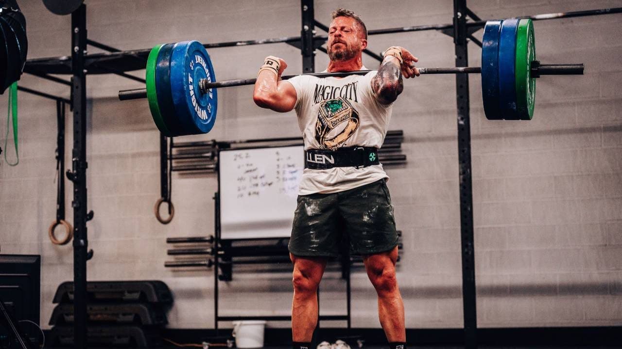 Jason Grubb with a barbell at his shoulders in a garage gym